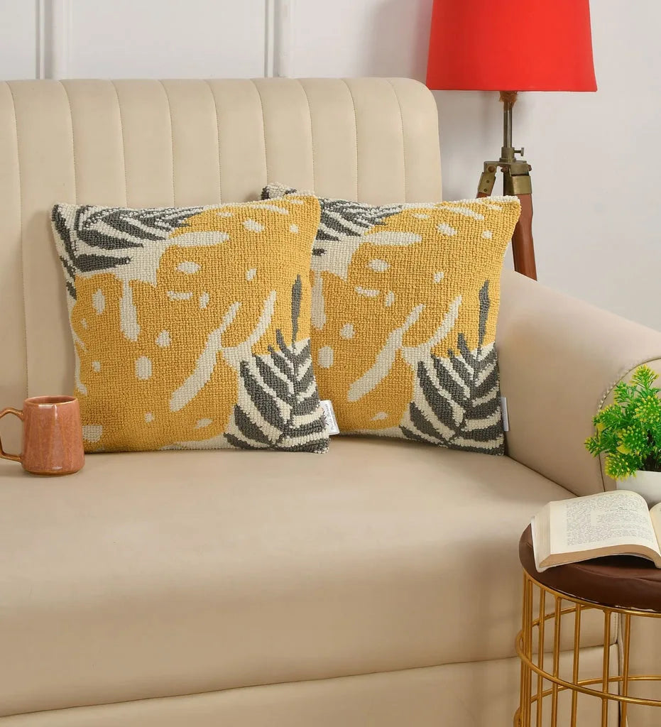 Decorative pillows with leaf patterns on a beige sofa with a red lamp and small table in the background.